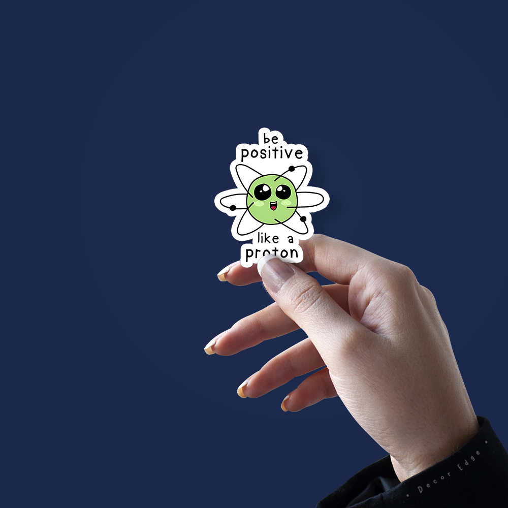 Hand holding a cute science sticker with green atom character saying be positive like a proton