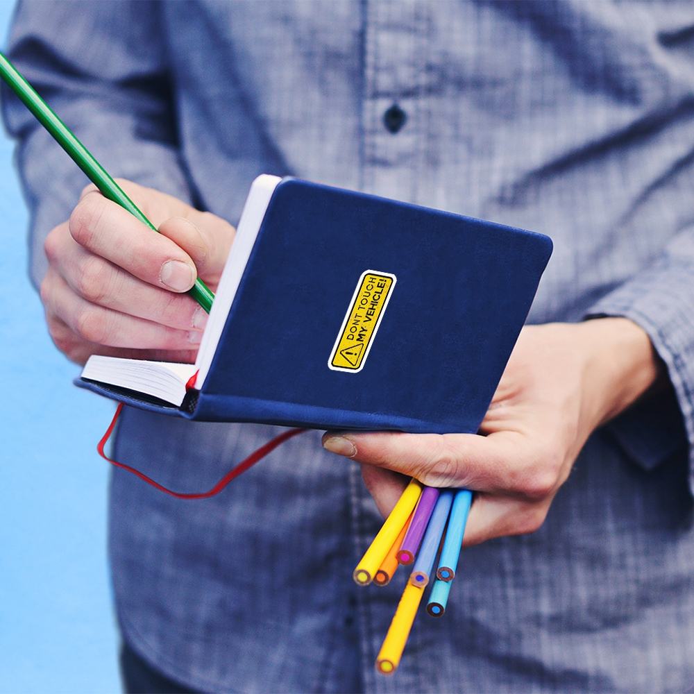 dont touch my vehicle sticker on blue notebook held by person writing with green pencil